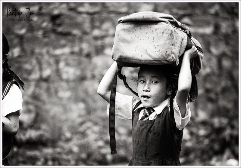 A little girl hold her school bag above her head during rains